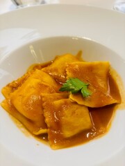 Handmade meat-filled ravioli served with a rich braised beef sauce. This traditional Italian dish is presented on a white plate, featuring tender pasta parcels and tomato and beef ragù