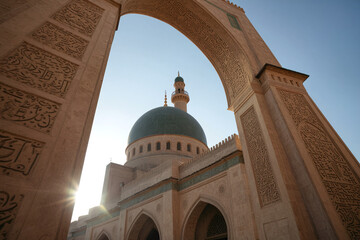 A looming beautiful archway with intricate Arabic inscription and patterns decorating the stone walls serving as an entrance of a grand Islamic mosque build during ancient times in the Middle East.