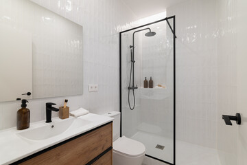 Modern bathroom with a glass shower, white tiles, wooden vanity, and minimalist decor. Clean and bright atmosphere with natural light.