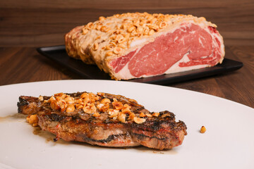 Fetta di carne appena cotta e guarnita con nocciole fotografata in un piatto bianco con il pezzo di carne crudo alle spalle