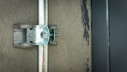 Close-up of metal conduit clamp with screw fixing electrical steel pipe to concrete wall in industrial installation.