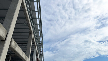 Fototapeta premium Concrete and steel building structure under construction with cloudy sky background, modern industrial architecture concept.