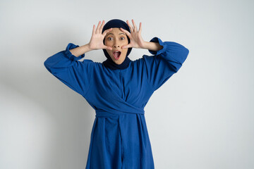 A surprised woman wearing a blue dress and hijab expressing astonishment with wide open eyes and...