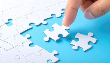 A hand places a white jigsaw puzzle piece among other pieces on a bright blue surface, near to completion, suggestive of problem-solving and strategy