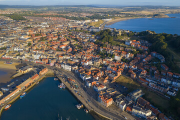 Obraz premium Aerial morning view of Scarborough town and harbour, with rows of colourful houses, fishing boats along the quayside, and sweeping views of the sandy bay and surrounding coastline.