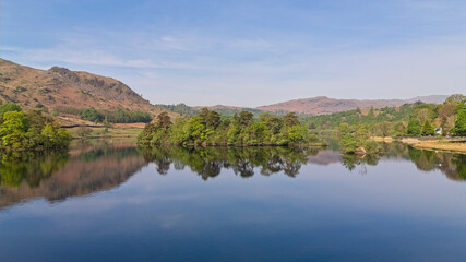 Obraz premium The tranquil Rydal Water lake reflects the surrounding hills and lush green islands beautifully.