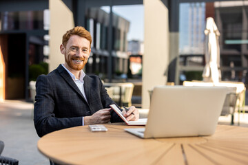 Businessman with red hair writing in diary at modern urban coffee shop