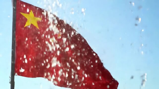 Slow motion video of the national flag of China waving proudly with splashing water drops against a clear blue sky