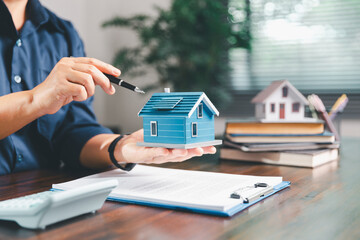 Female hand holds small miniature toy house, symbolizing woman dream of moving into her own...