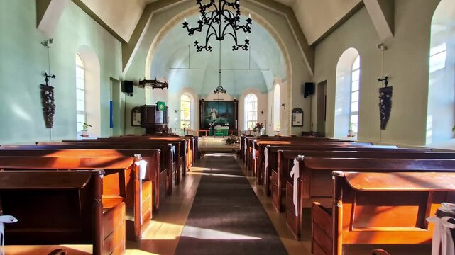 Warm morning light fills the wooden pews and arched windows inside Lielvārde church. Lielvārde, Latvia