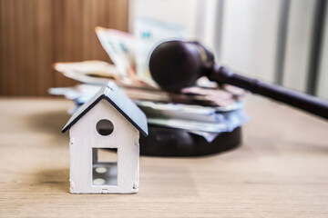 a model house placed in front of a judge's gavel and euro banknotes. Title, mortgage, debt...