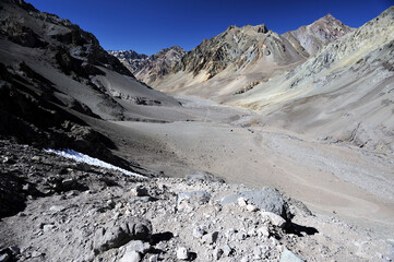 A sandy desert between gray mountains with snow on top. A river bed between the mountains. A view of desertification in a mountainous area.