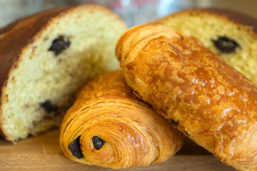 Golden loaf and flaky chocolate pastries on a wooden board, highlighting artisan bakery style and inviting texture.