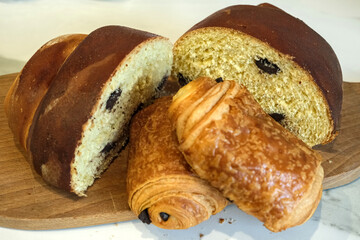 Golden loaf and flaky chocolate pastries on a wooden board, highlighting artisan bakery style and inviting texture.