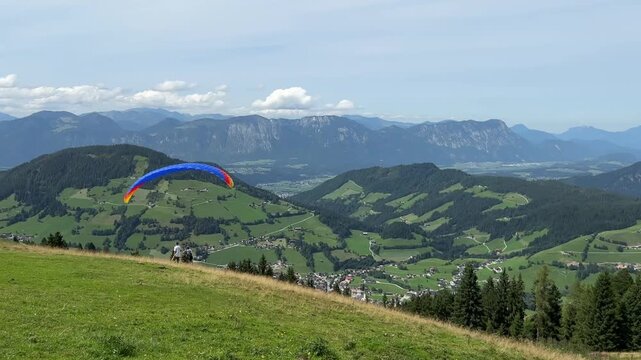 Majestic view of two paragliders against a mountain landscape. A red paraglider hovers in the air, while a blue one lifts off the ground and hovers, capturing the thrill of flight and adventure
