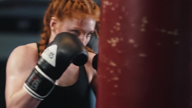 Determined female boxer intensely training with punching bag in a gym preparing to compete