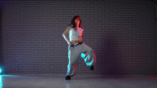 young crazy girl dancing hip hop against wall background in neon lighting, female choreographer moving to music and performing jazz funk in dance studio