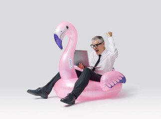 Obraz premium Cheerful businessman riding an inflatable toy and using a laptop