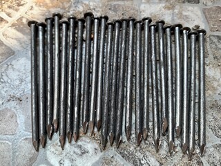 Close-up of sharp steel nails neatly arranged on rough stone floor, detailed texture with rustic...