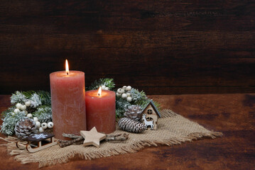 Rustic Advent and Christmas decoration: Two burning candles with fir branches and Christmas decorations in front of a wooden background with space for text.