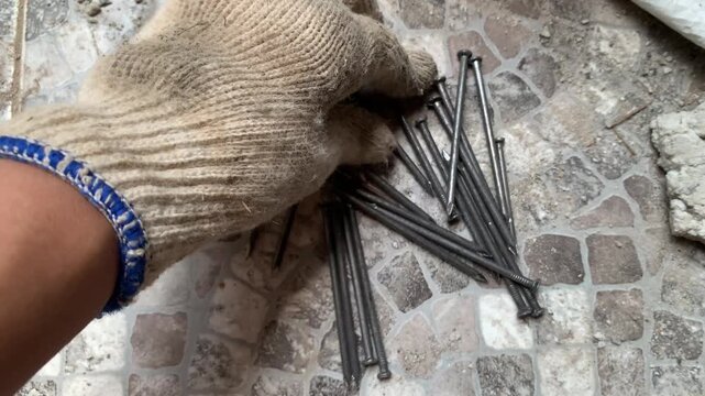 4k Close-up of worker hand in safety glove arranging scattered nails on stone floor. Focus on detail, texture, and labor mood. Great for construction, safety, repair, and industrial concepts.