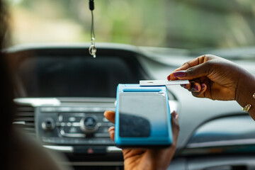 African woman making contactless credit card payment for transport fare using POS terminal inside a car.