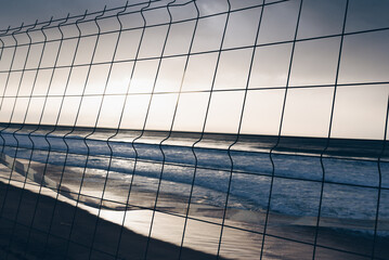 Sunset view of the ocean through a wire fence