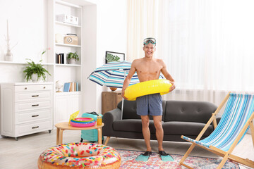 Happy man in flippers with diving mask and inflatable ring at home. Dreaming about vacation at sea