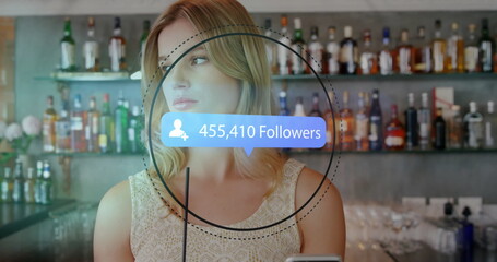 Posing influencer engaging with digital overlay at bar counter, with liquor bottles and straw glass
