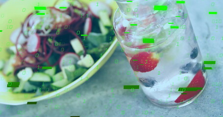 Displaying clear glass carafe holding ice water with berries on stone table, with green salad bowl