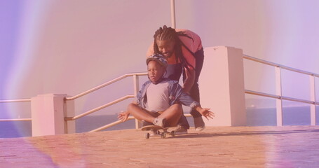 Pushing father guiding boy balancing skateboard on boardwalk, with safety helmet and metal railing