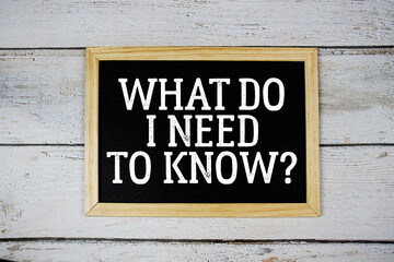 What Do I Need to Know? text with blackboard on wooden background