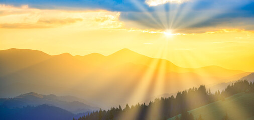 Beautiful sunset panorama in mountains. Landscape with sunset mountains and sun light through clouds