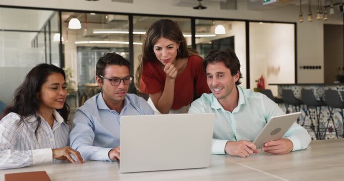 Four laughing team members gathered around laptop in modern coworking