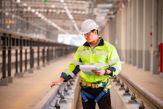Construction engineer inspecting railway track industrial documents in hand while examining rail structure closely construction, safety and professional project management transportation development.