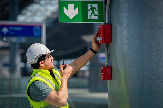 Safety engineer checking fire alarm system public building using a walkie-talkie inspecting emergency equipment an exit sign highlights workplace safety fire prevention and building maintenance.