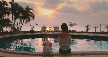 Tranquil beach resort with palm trees, calm ocean, and breathtaking sunset. Luxury spa swimming pool. Long hair caucasian brunette enjoy colorful sky and sea ocean scene. Back view,