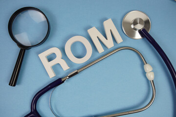 ROM abbreviation of Range Of Motion alphabet letters with magnifying glass and stethoscope on blue background