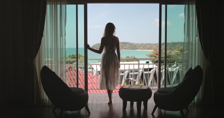 Woman elegance walking on balcony, enjoy ocean view from hotel room apartment, sunny day. Outdoor lifestyle travel on summer holiday vacation. Phuket tropical island, Thailand. Back view