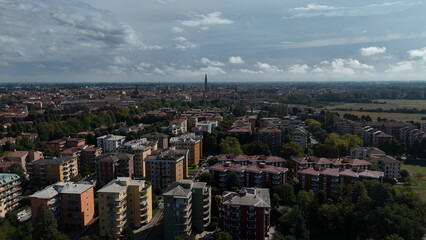 Drone aerial view of Cremona Italy capturing sprawling urban landscape Po River and industrial elements showcasing the citys architectural diversity and economic activity under a partly cloudy sky