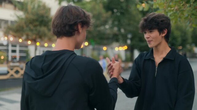 Two teens greeting each other outdoors in casual style with high five