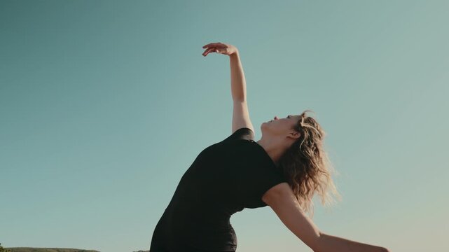 Elegant dancer gracefully moving outdoors with arm extended against a clear blue sky. Concept of freedom, art, and expression.