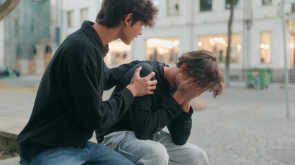 Sad teen comforted by his caring friend outdoors, symbol of true friendship