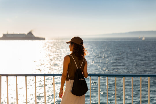 Jeune femme regard tourn&eacute; vers l'horizon de la mer, vue de trois quart arri&egrave;re, portant une casquette, se tenant sur la corniche Kennedy surplombant la mer, Marseille, Sud de la France