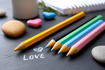 Naklejka premium Colorful pencils arranged on black background with love drawing 