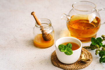 Pfefferminztee in einer Tasse und Honig in einem Einmachglas auf einem weißen Tisch. Teepause, Kräutermedizin.