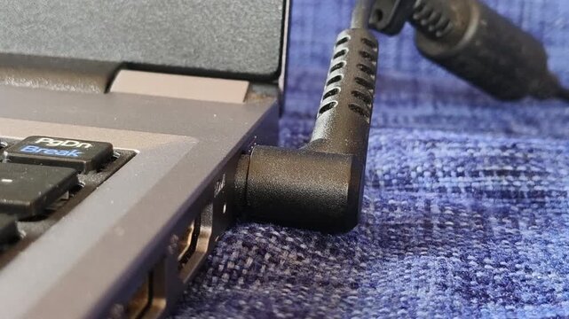 Closeup of hand connect power cable plug to laptop device charging port. Old or traditional computer power supply charger concept.