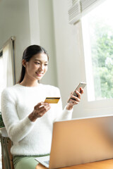 Young Asian woman enjoying a peaceful moment reading a book near window. Calm lifestyle, self-learning, and mindfulness at home.