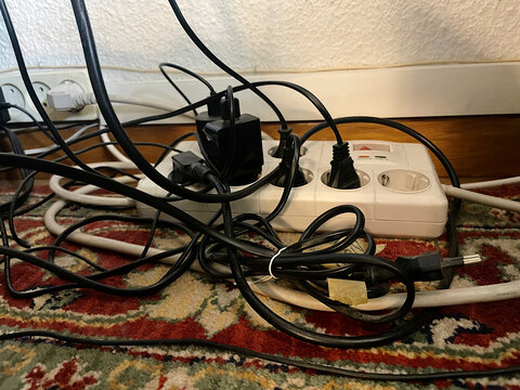 Lío de cables eléctricos enredados y enchufados en regleta base multicontacto sobre la alfombra del suelo del salón de casa