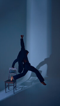 Male dancer stretching upward from chair in suit with extended arm and emotional strength. Concept of editorial menswear, resilience, performance art, and wordless storytelling.